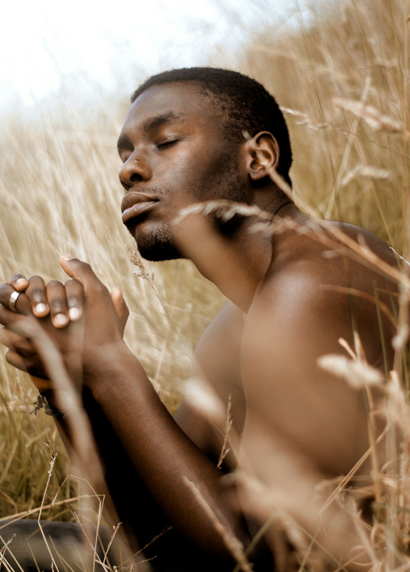topless Black man sitting on brown grass field during daytime